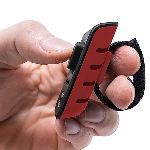 Hand holding a small red and black gadget with a strap